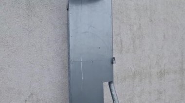 Koridorun çatısına çıkan yangın merdiveni koruyucu ızgaranın alt kısmındaki ızgarayla korunuyor. Beyaz metal depo duvarları. Galvanize demir ve yangın hortumunu bağlamak için bir boru.