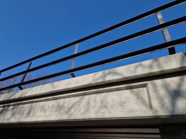 Demiryolu köprüsünde metal L profillerinden yapılmış metal korkuluklar. Köprünün altında güneşli güzel bir gün