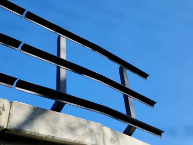 Demiryolu köprüsünde metal L profillerinden yapılmış metal korkuluklar. Köprünün altında güneşli güzel bir gün