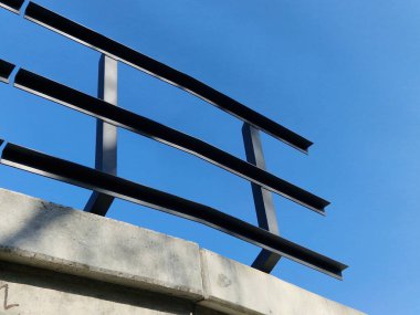 Demiryolu köprüsünde metal L profillerinden yapılmış metal korkuluklar. Köprünün altında güneşli güzel bir gün