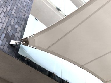 Beyaz tente gergin, güneşten gölgeleniyor ve restoranın terasında yağmur yağıyor, çocuk parkında, platformda. Direk ve gergin halatlar uçlarına sıkıca bağlanmış.