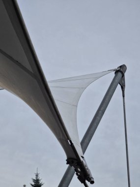 Beyaz tente gergin, güneşten gölgeleniyor ve restoranın terasında yağmur yağıyor, çocuk parkında, platformda. Direk ve gergin halatlar uçlarına sıkıca bağlanmış.