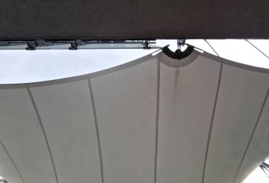 Beyaz tente gergin, güneşten gölgeleniyor ve restoranın terasında yağmur yağıyor, çocuk parkında, platformda. Direk ve gergin halatlar uçlarına sıkıca bağlanmış.