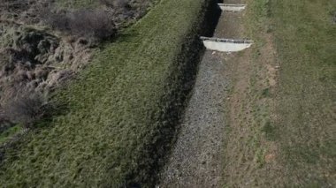 Köprünün altındaki kanalizasyon boruları. Yan yol hendeği geçiyor. Etrafı taşlarla çevrili beton bir delik. Yolun etrafındaki oluklar temiz su, yeni asfalt, kenar ve çakıl dolu.
