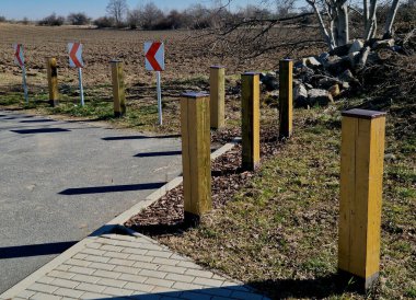 Tahta kirişlerden yapılmış kalın çizgiler. Araç girişine karşı önlem alan doğal park. Bollardın tepesinde metal bir çatı vardır.