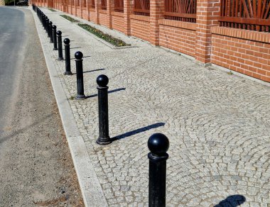 Kara metal kalınlar yaya bölgesindeki yayaları ya da gezinti alanındaki parktaki yayaları korumak için kullanılır. Gri sütunlar kaldırımdaki araçların park edilmesini engelliyor, çiçek tarhı, resmi şeritler