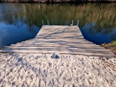 Park ziyaretçileri için iskele. İki adım ona götürür. Suyun üzerinde kalaslar var. Tekneler için rıhtımı olan bir gölet. Bir dikdörtgenin kat planı. Terasta parmaklık yok..