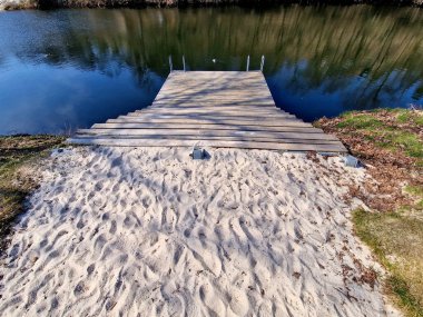 Park ziyaretçileri için iskele. İki adım ona götürür. Suyun üzerinde kalaslar var. Tekneler için rıhtımı olan bir gölet. Bir dikdörtgenin kat planı. Terasta parmaklık yok..