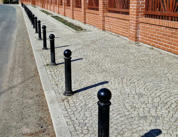 Kara metal kalınlar yaya bölgesindeki yayaları ya da gezinti alanındaki parktaki yayaları korumak için kullanılır. Gri sütunlar kaldırımdaki araçların park edilmesini engelliyor, çiçek tarhı, resmi şeritler
