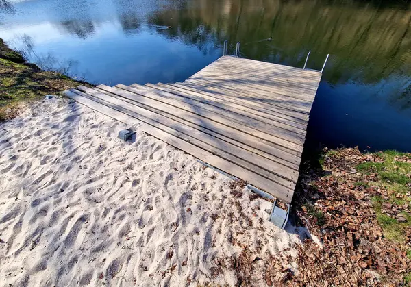 Park ziyaretçileri için iskele. İki adım ona götürür. Suyun üzerinde kalaslar var. Tekneler için rıhtımı olan bir gölet. Bir dikdörtgenin kat planı. Terasta parmaklık yok..