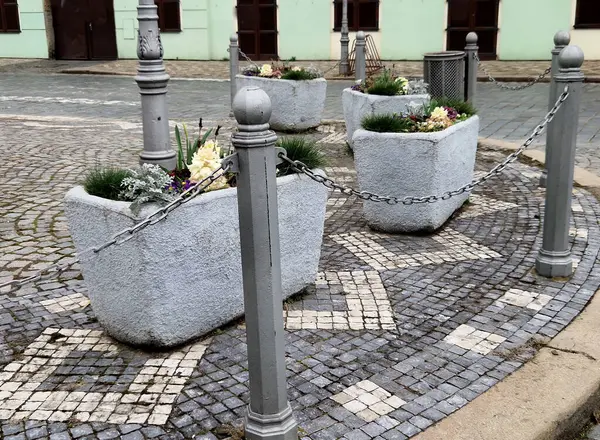 Yıllık çiçek tarlaları olan uzun ömürlü çiçek yatakları granit kaldırım taşı şehir meydanında kaldırım döşemeleri, girişte taş sütunlar ve taş yalaklar ve çiçek saksıları.