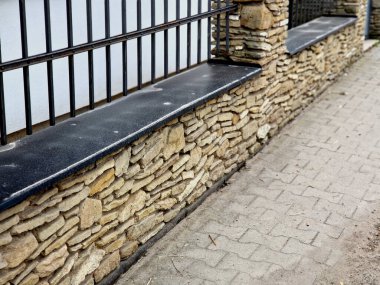 Düz taşlar sıra sıra dizilmiş duvarcılık çitleri oluşturur. Çatısı olan bir posta. Tarihi bir köy villasında ya da kulübesinde demir kafes işçiliği yapmış.
