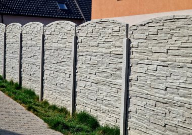Bahçede çimenli ve birbirine kenetlenmiş beton kaldırımlı gri çitli bir çit. Çit gürültüye karşı en iyi korumadır ve komşulara ve spor ayakkabılara karşı mahremiyet sağlar.