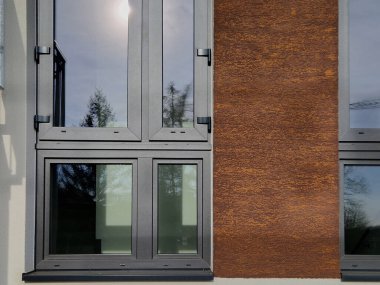 Gri renkli pencereli ve çerçeveli binanın duvarı. Ön cephe paslı kahverengi alçıdan yapılmıştır..