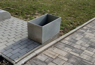 Şehir caddesinde gri plastik bir saksı. Bahçıvan toprağı ve bitkileri çiçeklerle ya da süslü çalılarla doldurur.