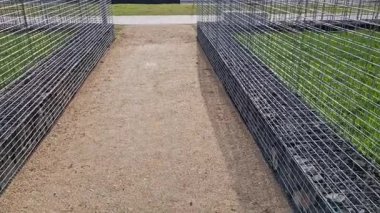 Bir apartman bloğundaki bahçeler arasında kıvrımlı duvarlar. Çakıl parkı yüzeyi olan halka açık bir yola açılan metal kapılar. Gabion sepetlerinde istiflenmiş taşlar