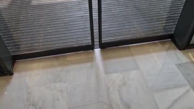 Binanın girişindeki endüstriyel paspas temizleme bölgeleri. Kemer ya da yarım daire şeklinde siyah plastik bir minder kireçtaşı mozaik fayansların üzerinde yatar.