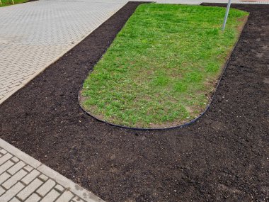 Siyah plastikten yapılmış bahçe kaldırımları. Kaldırım çimenleri ve çiçek tarlalarını ayırır, böylece temiz bir arayüz oluşur ve çimenler çimenlik malzemeleriyle bir çiçek tarlasına dönüşmez.. 