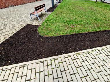 Siyah plastikten yapılmış bahçe kaldırımları. Kaldırım çimenleri ve çiçek tarlalarını ayırır, böylece temiz bir arayüz oluşur ve çimenler çimenlik malzemeleriyle bir çiçek tarlasına dönüşmez.. 