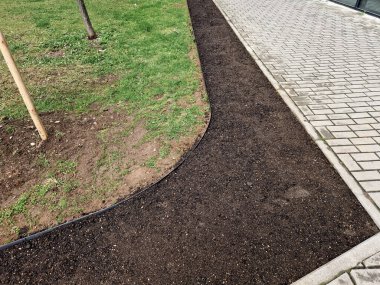 Siyah plastikten yapılmış bahçe kaldırımları. Kaldırım çimenleri ve çiçek tarlalarını ayırır, böylece temiz bir arayüz oluşur ve çimenler çimenlik malzemeleriyle bir çiçek tarlasına dönüşmez.. 
