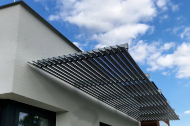 Pencerenin üstünde pencereleri güneşten koruyan çizgili bir panjur şeridi var. Binanın ön cephesinin güney tarafında..