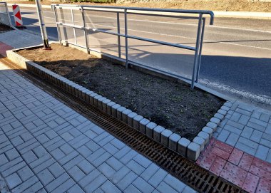 Otobüs platformu bir tarafında gri metal bir tüp korkuluğuna bağlı şeffaf pleksiglass ile korunuyor. İnsanlar geçen arabalardan, işlek caddeden, şoförden, su birikintisinden, kamuflajdan, kalkanlardan toprak püskürtülmez.