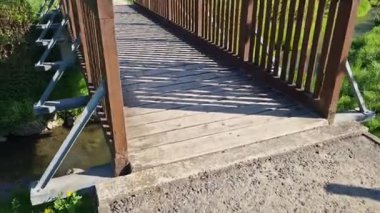 Ahşap korkuluklu bir park köprüsü dereyi geçiyor. Kirişler beton bir temeli tutan çelik bir kirişe sabitlenmiş. Köprü bariyerinin önünde çakıldan yola