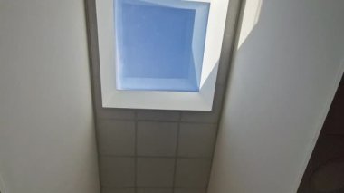 Başının üstünde dikdörtgen bir pencere var. Koridorun tamamını doğal ışıkla aydınlatıyor. Pencere dikdörtgen bir tavan penceresi. Duvarlar bembeyaz.