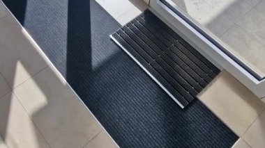 Binanın girişindeki endüstriyel paspas temizleme bölgeleri. Kemer ya da yarım daire şeklinde siyah plastik bir minder kireçtaşı mozaik fayansların üzerinde yatar.