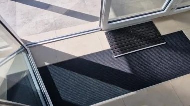 Binanın girişindeki endüstriyel paspas temizleme bölgeleri. Kemer ya da yarım daire şeklinde siyah plastik bir minder kireçtaşı mozaik fayansların üzerinde yatar.