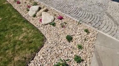 Uzun ömürlü çiçek tarhı, gri granitten yapılmış taşlar, şehir bahçesinde saman taşları, çayır, süs otları, havuzun kenarında çimenlik çakıl taşları.