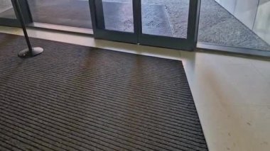 Binanın girişindeki endüstriyel paspas temizleme bölgeleri. Kemer ya da yarım daire şeklinde siyah plastik bir minder kireçtaşı mozaik fayansların üzerinde yatar.