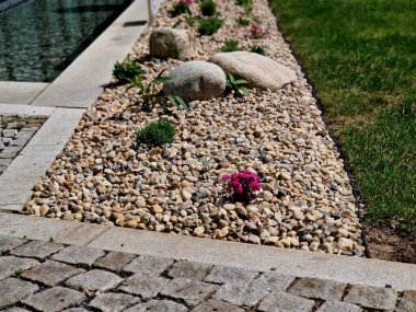 Uzun ömürlü çiçek tarhı, gri granitten yapılmış taşlar, şehir bahçesinde saman taşları, çayır, süs otları, havuzun kenarında çimenlik çakıl taşları.