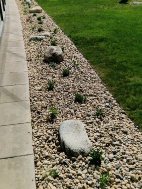 Uzun ömürlü çiçek tarhı, gri granitten yapılmış taşlar, şehir bahçesinde saman taşları, çayır, süs otları, havuzun kenarında çimenlik çakıl taşları.