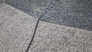İletişim işçileri yolun altına kablo gömüyor. Bir çakıl tabakasının altına geçici elektrik uzatma kablosu yerleştirilmiş. Hatalı bulgu. Bir adam güzergahı takip ediyor ve hasar arıyor..