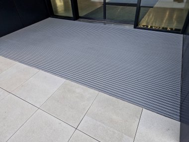 Keçeli mendil, kaset fırçası, gri alüminyum. Profiller asfalt seviyesinin altına gömülmüş. Değiştirilebilir keçeli kalemler ayakkabıları temizler ve suyu emer. Kayma riski azaldı.