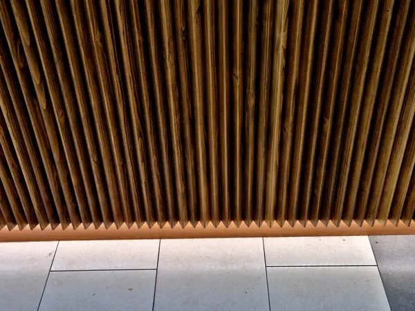 Dükkanın duvarındaki üçgen ahşap kalasların çentik tasarımı. Duvarın altında fayansların üzerinde parlayan bir LED ışıklandırma şeridi var.