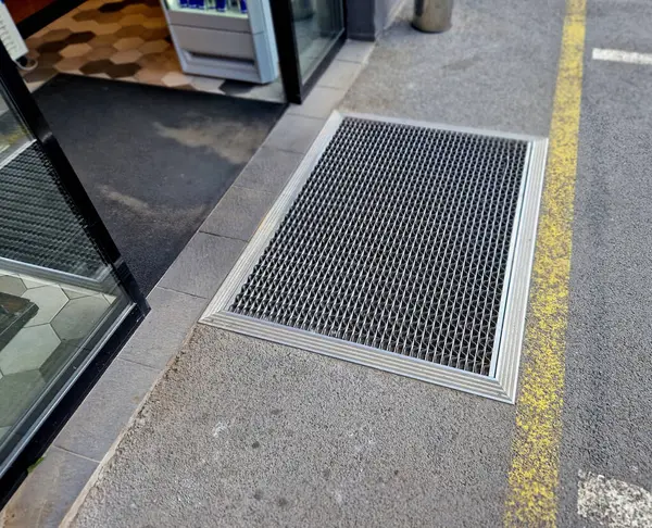 Keçeli mendil, kaset fırçası, gri alüminyum. Profiller asfalt seviyesinin altına gömülmüş. Değiştirilebilir keçeli kalemler ayakkabıları temizler ve suyu emer. Kayma riski azaldı.