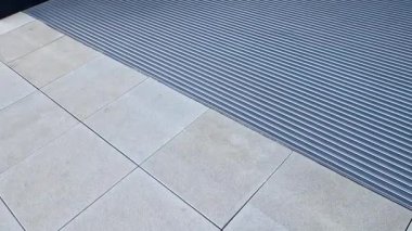 Keçeli mendil, kaset fırçası, gri alüminyum. Profiller asfalt seviyesinin altına gömülmüş. Değiştirilebilir keçeli kalemler ayakkabıları temizler ve suyu emer. Kayma riski azaldı.