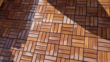 Pergola yakınlarında ahşap ızgara parkeden bir teras. Yumuşak kahverengi zig zag kare katlanmış rkna tabanı. Balkonda beyaz bir saksı