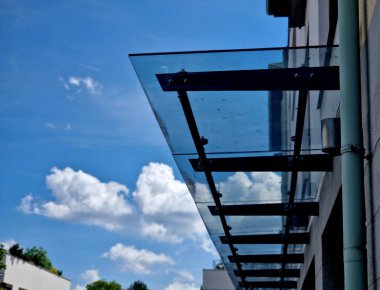 Endüstriyel binanın girişinin üstündeki cam çatı cephesinde metal kaplama var. Kalın duvarlı cam panel, metal çubuklarda, yuvarlak hedef tutucularla kapının üzerinde asılı.