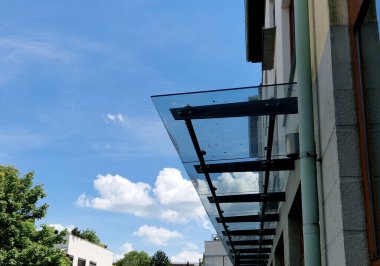 Endüstriyel binanın girişinin üstündeki cam çatı cephesinde metal kaplama var. Kalın duvarlı cam panel, metal çubuklarda, yuvarlak hedef tutucularla kapının üzerinde asılı.