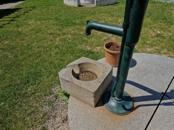 Parlak, parlak taş kapaklı. Bir el pompasından su, su olukları olan bir taş oluğa akar. Saf taş üretimi. özel bahçe ve park mimarisi