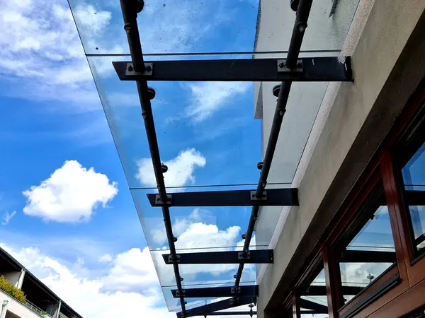 Endüstriyel binanın girişinin üstündeki cam çatı cephesinde metal kaplama var. Kalın duvarlı cam panel, metal çubuklarda, yuvarlak hedef tutucularla kapının üzerinde asılı.