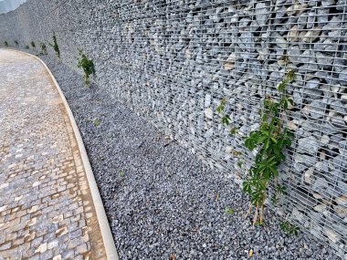 Yolun yamacını tutan çirkin beton duvar doğal taşlarla dolu bir gabionla kaplı. Astarın görünümü daha doğal.