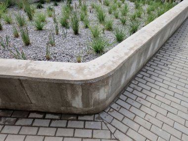 grass bed on the promenade. on the edge of the flower bed are pillar lamps with a beveled top. striped pavement on the promenade. grasses have dry stems like hair