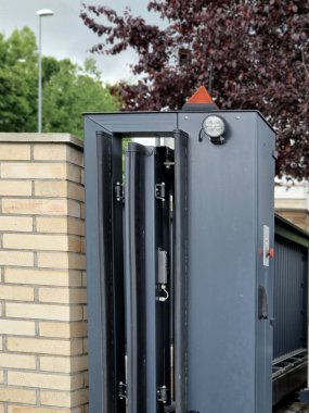 entrance to the yard to the parking lot through a low sliding gate. the gate moves sideways along the rail. there is an orange flashing beacon on the post. the remote control turn sliding gate, black