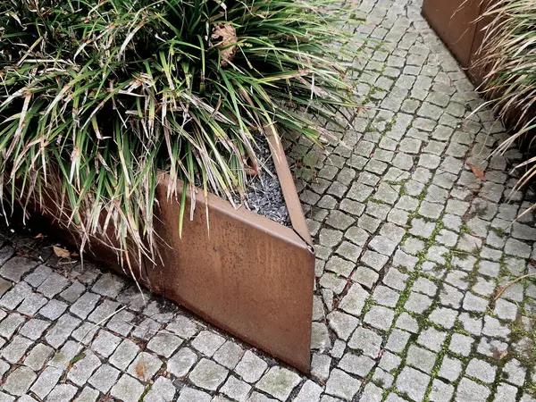 Çiçek tarlası paslı metal bir yaprak dizaynı ile sınırlıdır. Çiçek tarlasında uzun ömürlüler ve çimenler çiçek açar. İki çiçek tarhı arasında taş küpler. Bunlar banklar.