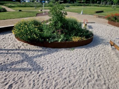 Çiçek tarlasının oval elipsi paslı metal bir levha ile kaplıdır. Uzun ömürlüler çiçek açıyor. Park özellikleri ve çocuk parkı olan kum havuzu. yuvarlak kenar, basamak, beton