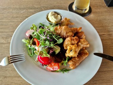 Bira hamuruyla kaplanmış balık ya da tavuk parçaları. Yan yemek olarak yapraklı sebze salatası. Buğday biralı ahşap masa. Lüks yaz yemeği.